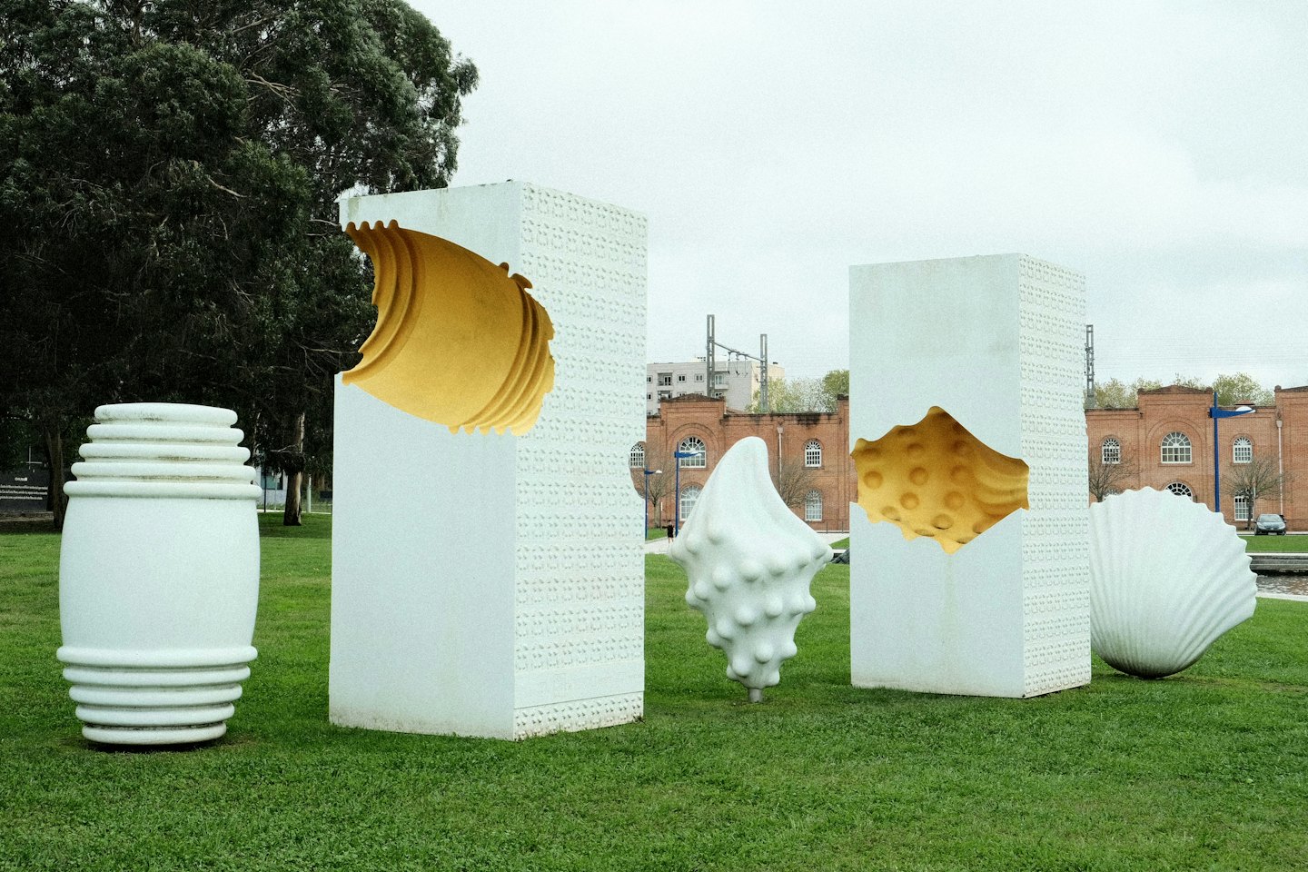 Abstract white and yellow sculptures stand on a green lawn.
