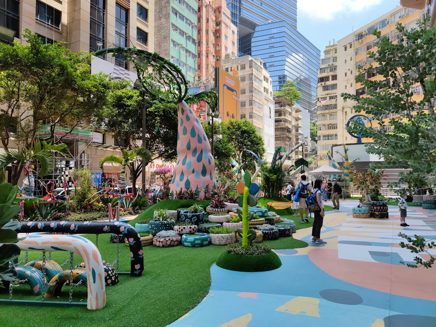 People walk through an urban park with colorful art sculptures.